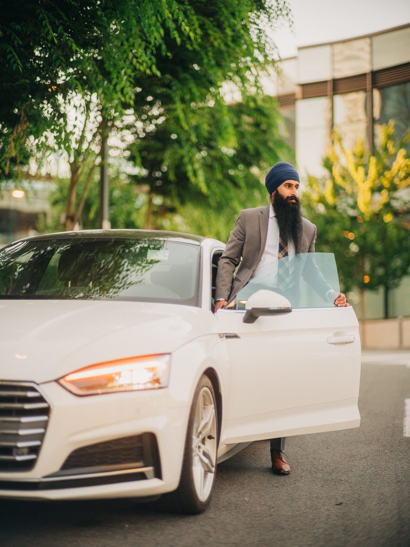 A man stepping out of his white car on a leafy street